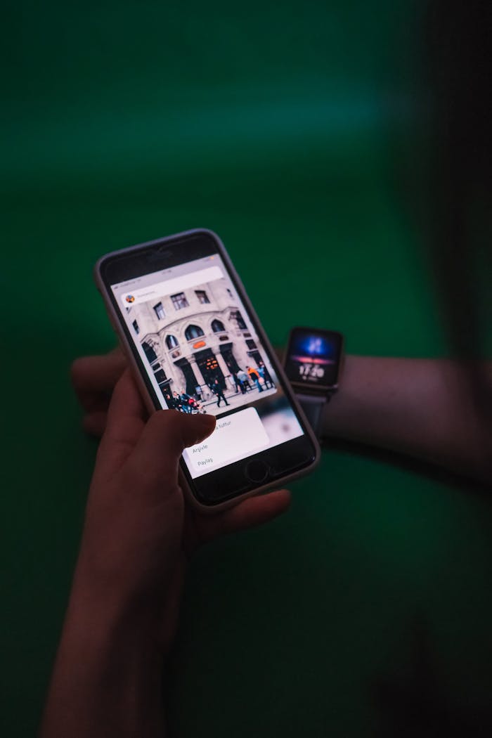 Close-up of a person using a smartphone and smartwatch indoors against a green background.